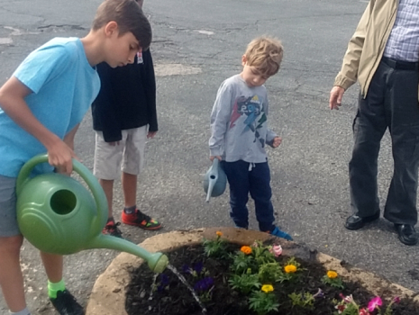 Children of UTRS employees watering flowers planted around 9/11 memorial at office