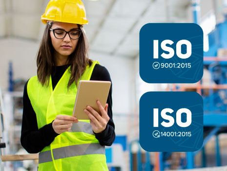 Woman in hard hat and safety vest inspecting warehouse with ISO logos to the right