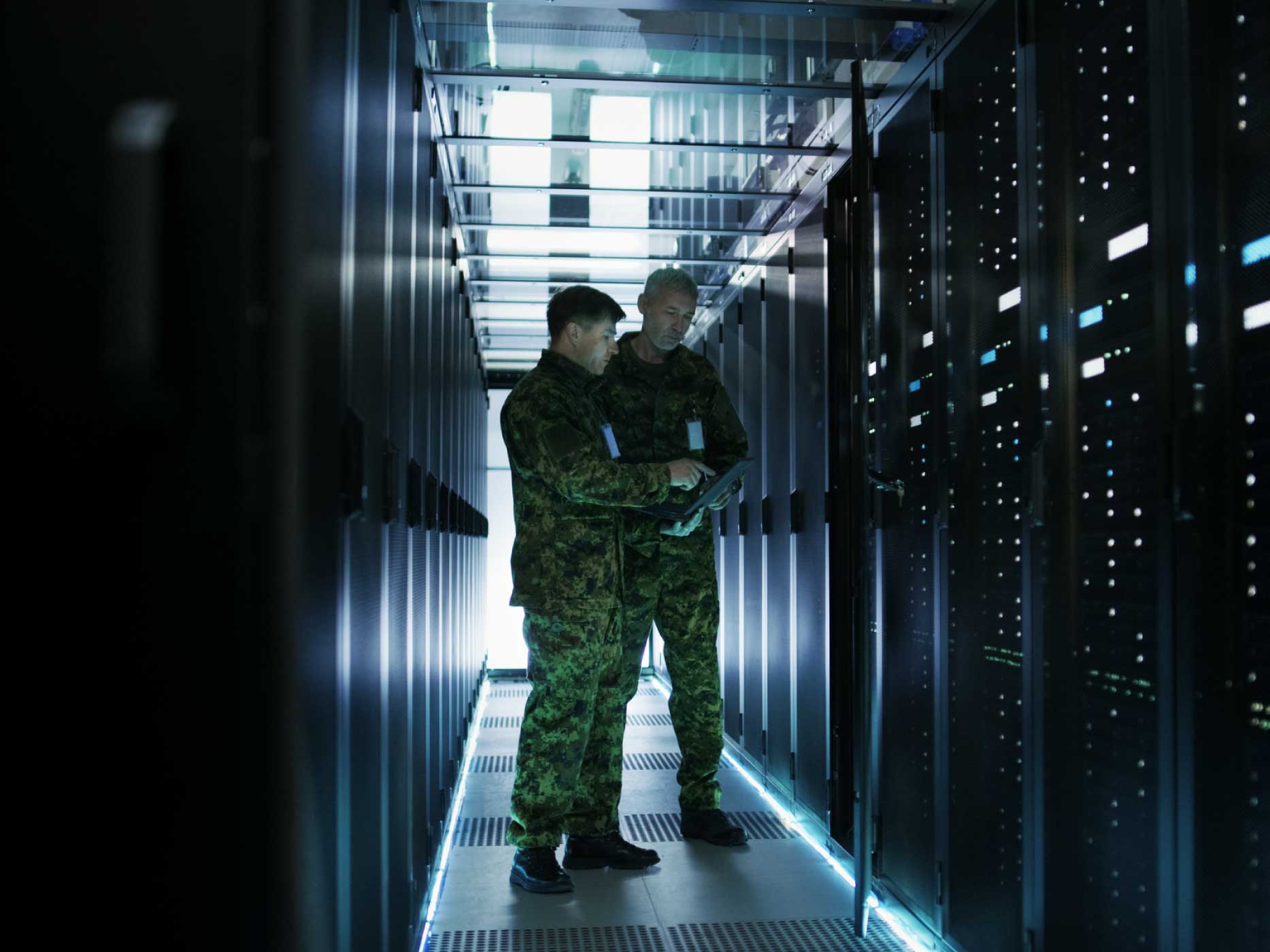 In Data Center Two Military Men Work with Open Server Rack Cabinet. One Holds Military Edition Laptop.