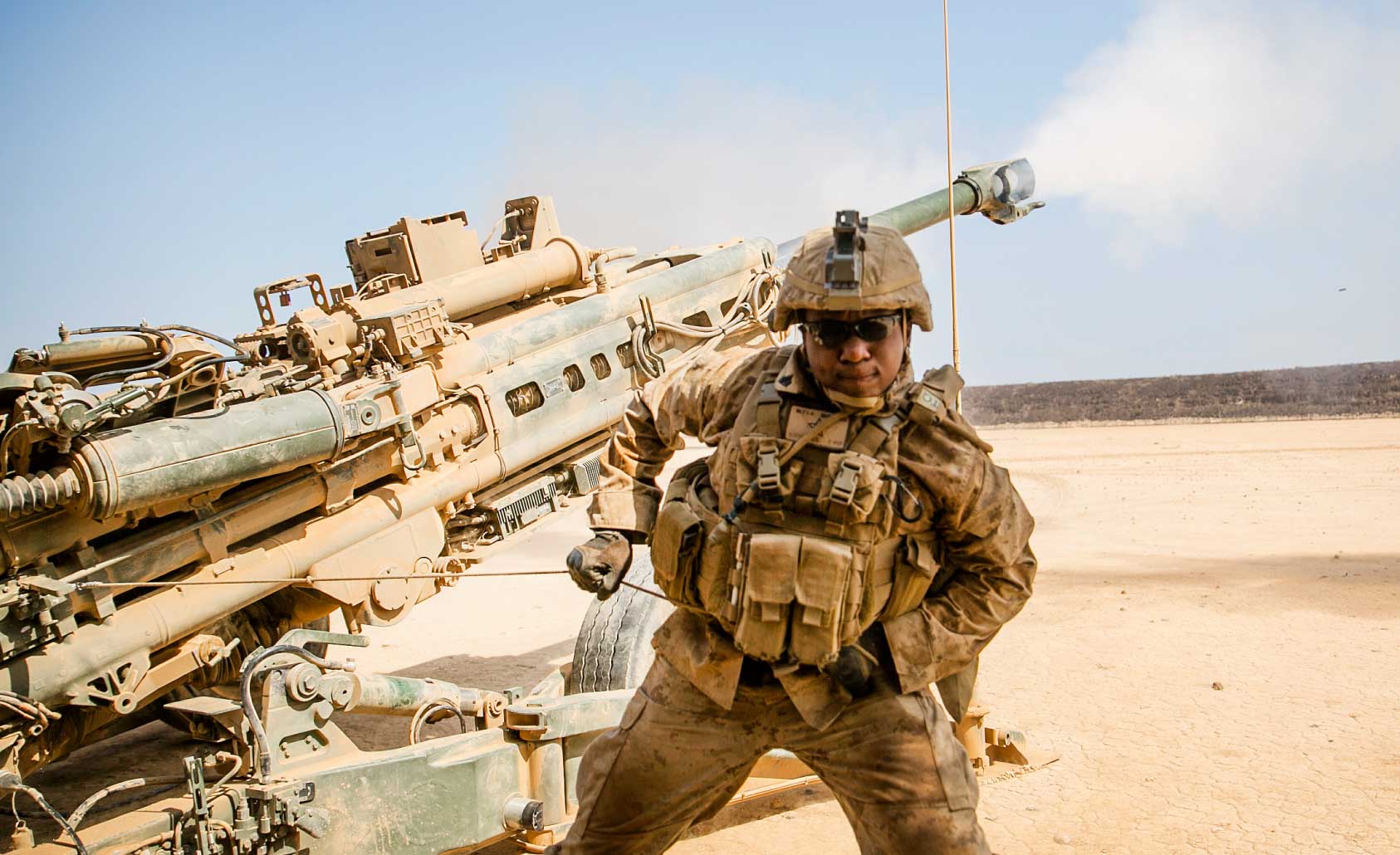 Marine pulls the lanyard firing a howitzer in a desert background